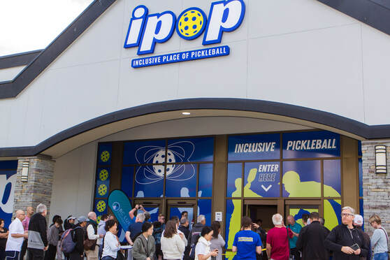 Crowd of people gathered outside the entrance of an indoor pickleball facility with ipop signage above the door.