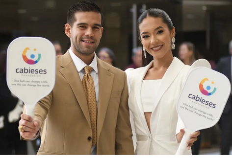 Man and woman in business attire holding cabieses-branded pickleball paddles and smiling at the camera