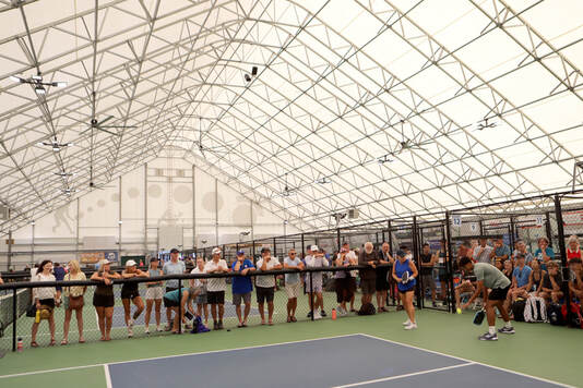 Indoor pickleball court with players and spectators watching a match under a large white tent structure