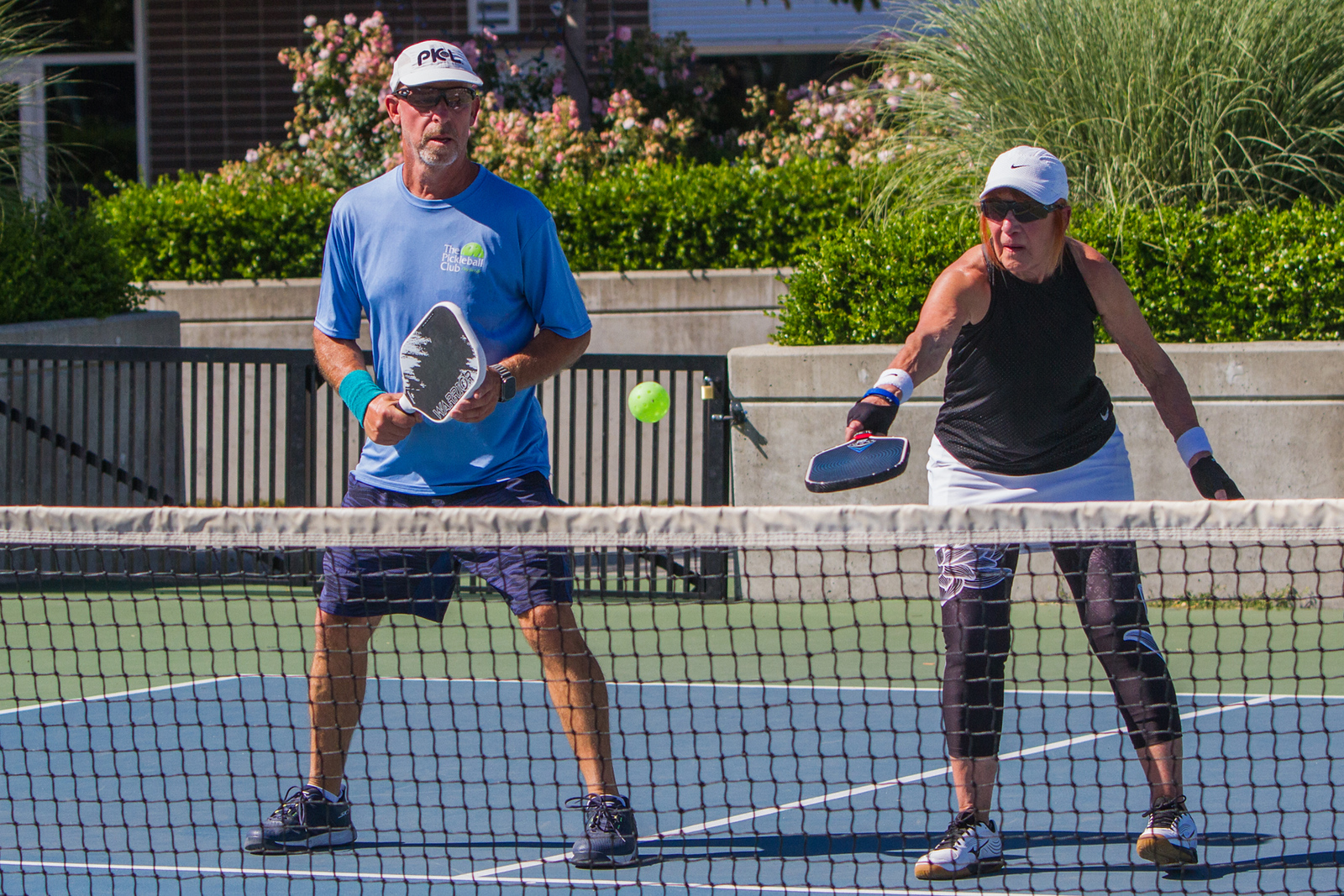 Two adults playing pickleball on an outdoor court, one hitting a ball over the net with paddles in hand.